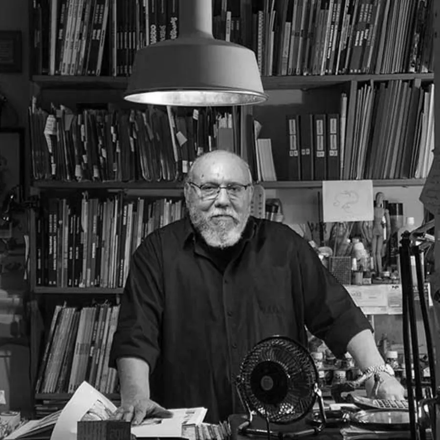 Retrato en branco e negro de Carlos Giménez diante de estanterías de libros