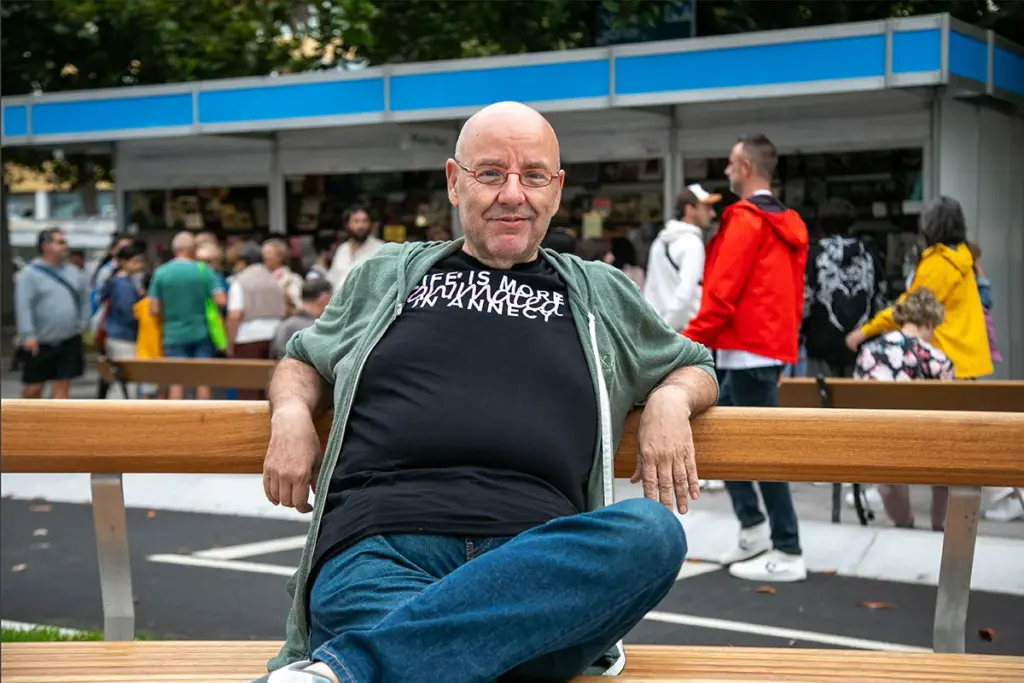 Raúl García sentado nun banco frente as casetas da feira