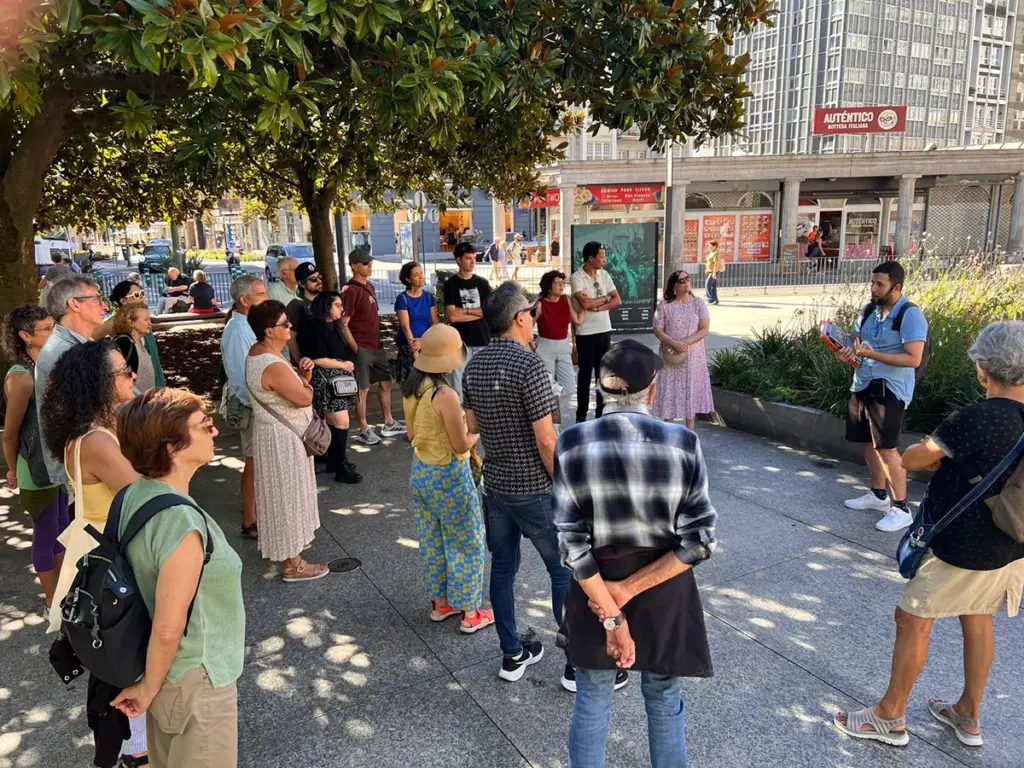 Persoas escoitando as explicacións do roteiro da memoria na praza Pontevedra da Coruña